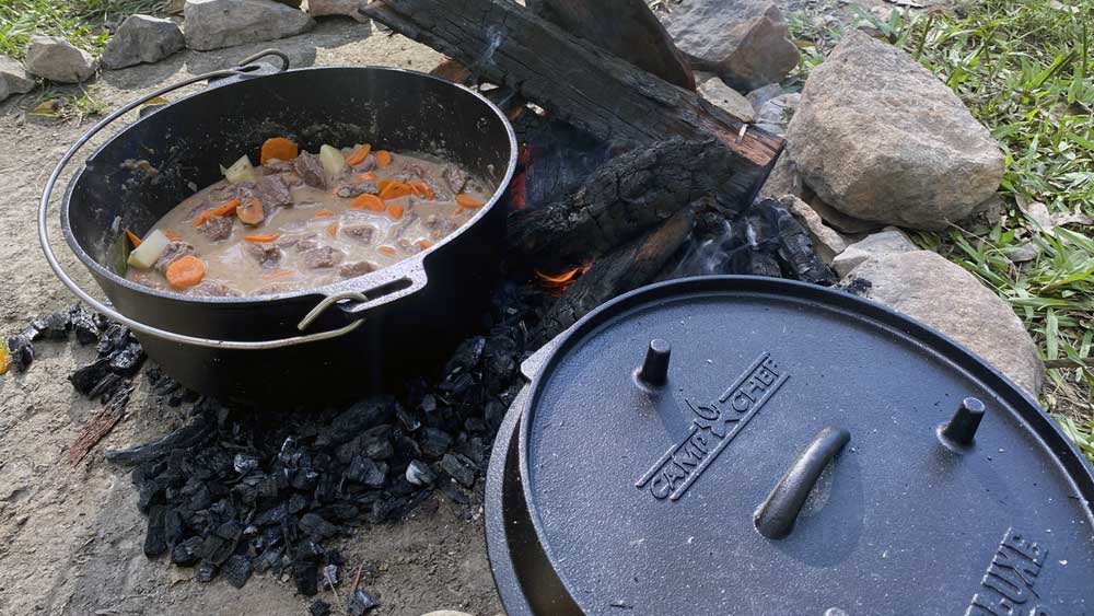This photo shows a beef stew cooking in a camp chef branded camp oven on a bed of coals at cobb and co nine mile campground, it's one of our favourite camp oven recipes to cook.